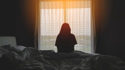silhouette of woman sitting on the bed beside the windows with sunlight in the morning