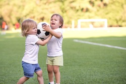 Two little toddlers arguing at football field or playground over soccer ball trying to take or grab ball. Conflict management, corporate fight metaphor and conflict resolving concept. Copy space