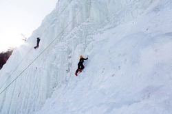 Low angle side view of two ice climbers on steep frozen cliff seen during a beautiful sunny winter day in the Montmorency Falls Park, Quebec City, Quebec, Canada