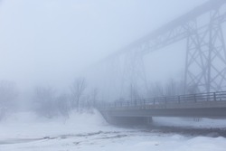 Overpass seen in dense fog over a river during a late winter morning, with 1908 trestle bridge in the background, Cap-Rouge area, Quebec City, Quebec, Canada