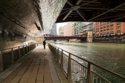 Man in silhouette strolling on Chicago river walk under a bridge