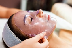 The beautician applies a transparent jelly peer mask to the girl's face. Facial skin care. 
