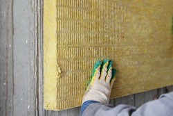 A builder attaches a rock wool slab to the wall with cement glue. Thermal insulation of buildings during construction