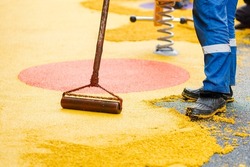 Worker leveling and pressing rubber coating for playgrounds with roller, mason hand spreading soft rubber crumbs. Outdoor soft coating and floor covering for sports. Selective focus.