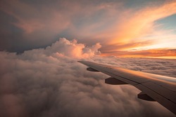 The view from the airplane window to the clouds and sunset. Airplane wing above thick pink and orange clouds. Wonderful breathtaking view.