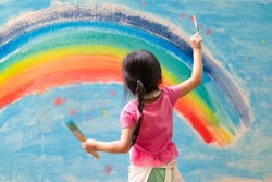 Unidentified little girl is painting the colorful rainbow and sky on the wall and she look happy and funny, concept of art education and learn through play activity for kid development.	