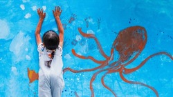 Unidentified little girl is messy painting the wall of ocean world and sea animals, and paint hand and arm with water color, concept of free play and art activity for kid at home for child learning.