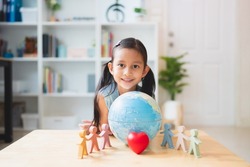 Asian little girl smiling behind the people, heart, globe model play toys, concept of diversity, inclusion, unity, equality, peaceful, love, connection, and friendship of people around the world.