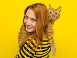 Young foxy woman in yellow cardigan loves her cute ginger cat Cat. Yellow background
