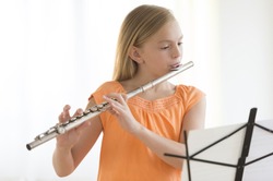 Little girl looking at sheet music while practicing flute at home