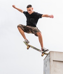 Young skateboarder in shorts jumping a wall in an urban environment.