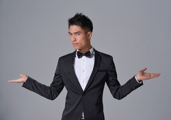 Handsome fashion model.
elegant man wear formal black suit with bow tie ,open hands on gray background 

