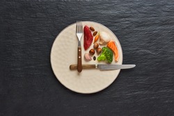  20:4 fasting diet concept. One third plate with healthy food and two third plate is empty. Beef, salmon, egg, broccoli, tomato, nuts, carrots, mushrooms. Dark background. Top view.