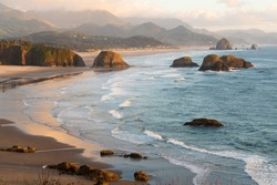 Late evening sunlight falls across Cannon Beach and the sea stacks on the Oregon Caost alongside the Pacific Ocean