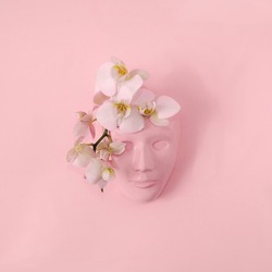 A pastel pink women's head  of plaster with fresh white and pink orchids on the forehead on pink background. Romantic surreal creative concept for spring summer fashion vision. Minimal conceptual art