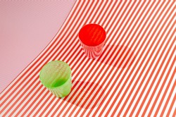 A green and a red glass on red and white striped asymetric background with shadows. Minimal artistic concept for summer drinks in the sun.
