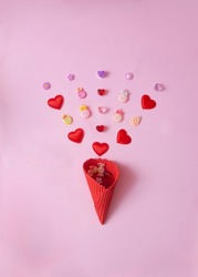 Red hearts and pastel colored candies coming out of a bright red ice cream cone against pink background. Creative concept for Valentine card. Design for engagement or wedding announcement. Flat lay