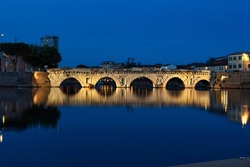 Rimini, Emilia Romagna, Italy: ancient Roman bridge of Tiberius at night after sunset with city lights, dark blue sky