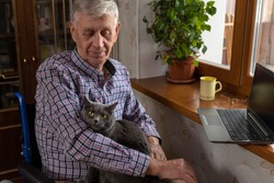 An elderly man is at home, hugging his favourite cat sitting on his lap.