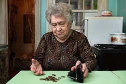 A sad old woman counts money at home in the kitchen. The concept of poverty, old age, poor lifestyle of the elderly. 