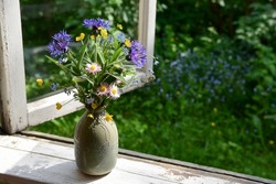 Bouquet of summer wildflowers in a vase on a wooden window sill. Still life on the window of an old country house, summer cottage.