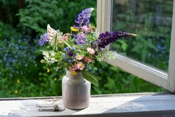 Bouquet of wild flowers in a vase on a wooden window sill. Still life on the window of an old country house, summer cottage. Floral home decoration. 