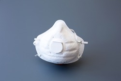 A non reusable non sterile white ffp3 / N95 mask with valve that can be used as protection against viruses such as covid-19 corona virus, h1n1, h5n1 shot on a grey background
