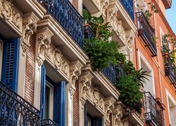 Facade of historical buildings in Madrid, Spain, Europe. Ornaments and balcony with lush green plants. Colorful Mediterranean street scene in Lavapiés, Embajadores neighborhood of the Spanish capital.