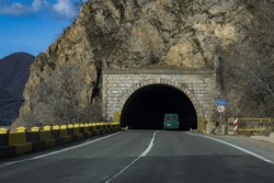 A car (van) at the entrance of a road tunnel. The road tunnel crosses the mountains.