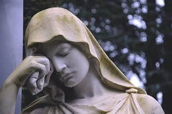 Detail of a cemetery. Statue of a sad virgin Mary as a symbol of depression pain and sorrow. Sad crying Madonna as Tombstone in a cemetery.