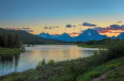 Oxbow Overlook. The sun sets behind the Grand Tetons and is reflected in the Snake River.