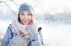 Beautiful  happy laughing young woman wearing winter hat gloves and scarf covered with snow flakes. Winter forest landscape background