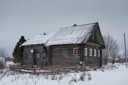 Traditional village house in winter in cloudy weather. Old northern residential architecture of Russia. Log cabin is called izba