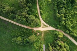 Top view of the dirt road with a crossroads and dense green forests. Beautiful bright landscape photography with drone on a summer day
