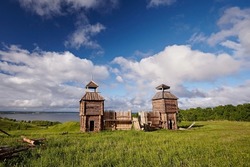Beautiful wooden fortress made of logs with a tower against the background of the summer landscape and blue sky with white clouds. Traditional Old Architecture of the Middle Ages North