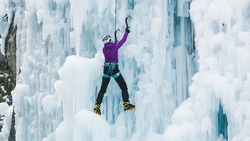 Woman climbing on a frozen waterfall in technique front-pointing with one foot and flat-footing with the other
