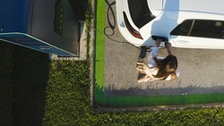 Bird's eye view shot of a young Caucasian woman charging a white electric car at a private EV charging station