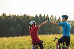 Woman and a man on racing road cycles taking a break after successful training and looking at sunset over mountains giving high five