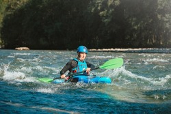 Male recreational athlete paddling carefully over the risky, foamy, and splashy whitewater rapids in his blue kayak