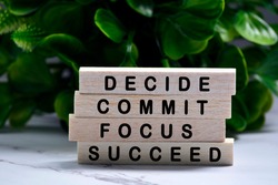 Inspirational words of decide commit focus succeed on wooden blocks with green background
