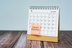 April calendar on wooden desk with date circle and text on sticky note. Easter Sunday on 17th April 2022.