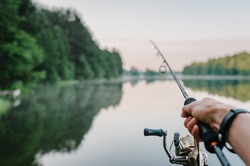 Fisherman with rod, spinning reel on the river bank. Sunrise. Fishing for pike, perch, carp. Fog against the backdrop of lake. background Misty morning. wild nature. The concept of a rural getaway.