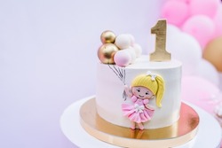 Birthday cake for 1 year. The cake is decorated with a doll figure and decor for the girl. Delicious reception at a birthday party. Trendy cake on the background of balloons.