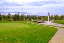 Landscape. Hills with green lawn and ornamental shrubs and trees lake fountain and bridge. Beautiful garden