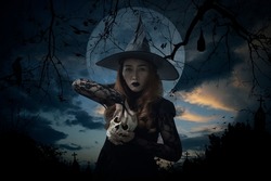 Halloween witch holding a skull standing over cross, church, crow, bat, birds, dead tree, full moon and sunset sky, Halloween mystery concept