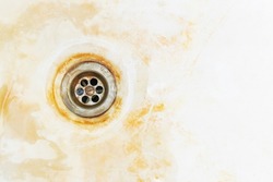 An old rusty bathtub surface with a metal drain hole. Dirty cracked unclean bath or sink with red rust stain, close-up. Corrosion, unsanitary concept, copy space.