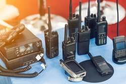 Many portable radio transceivers on table at technology exhibition. Different walkie-talkie radio set. Communication devices choice for military and civil use