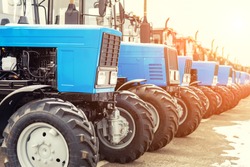 Many different tractors standing in row at agricultural fair for sale outdoors.Equipment for agriculture.Heavy industrial machines presented to an agricultural exhibition