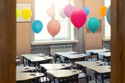 Entrance door of empty elementary primary school interior furniture children desk decorated with multicolored colorful air balloons against window. Happy knowledge day and back to school concept