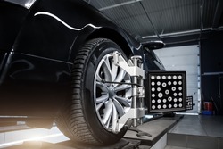 CLose-up car wheel indoors service maintenance repair center against laser sensor equipment diagnostics and 3d wheel alignment. Vehicle inside garage workshop for auto camber toe check fixing work